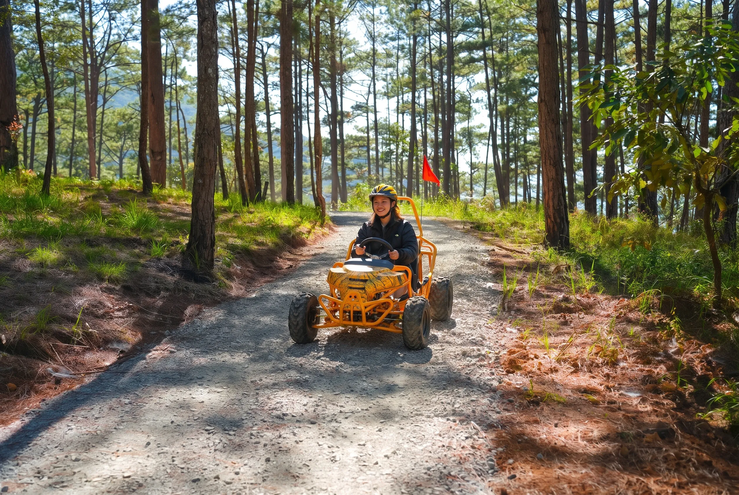 A smiling woman in a helmet driving an orange-yellow off-road kart along a gravel track through tall pines
